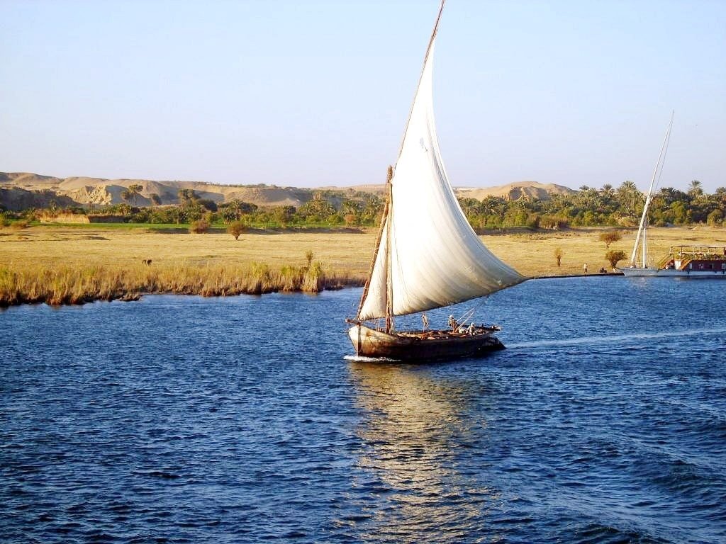 Eine traditionelle Feluke segelt sanft auf dem blauen Nil bei Sonnenuntergang